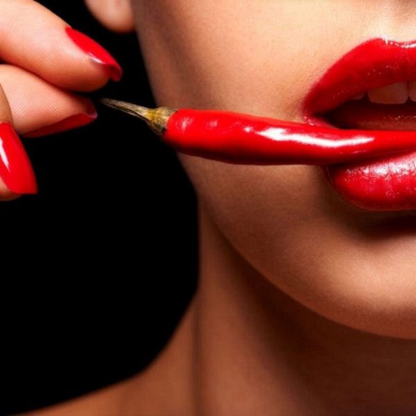 Mulher com pimenta vermelha junto aos lábios representando aromaterapia biológica afrodisíaca