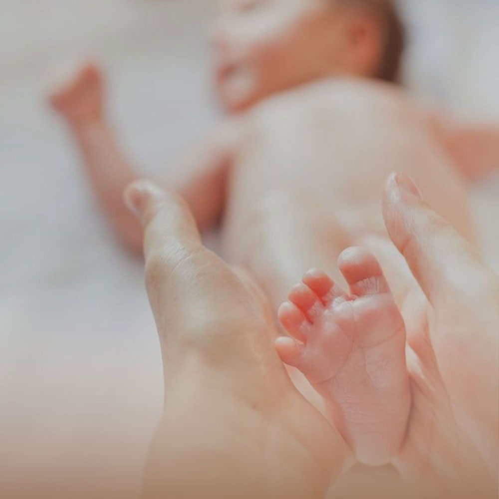 Pé de bebé segurado por mãos adultas representando aromaterapia em pediatria